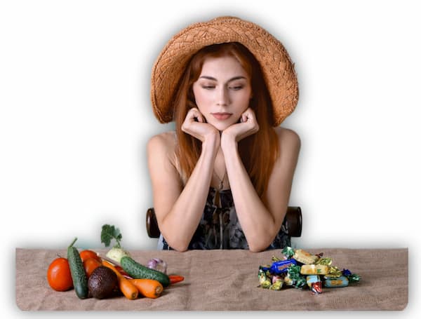 A contemplating women with vegetables on one side of the table and candies on other