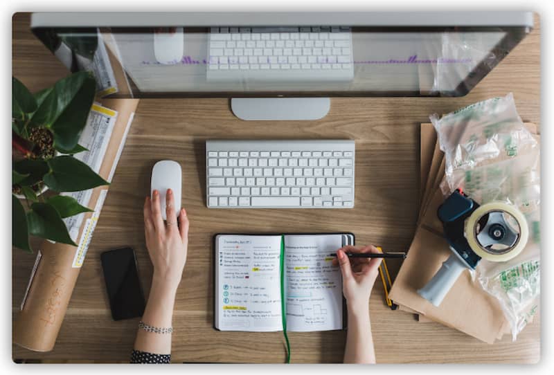 A top view of a multitasking person scrolling mouse while taking notes on a diary