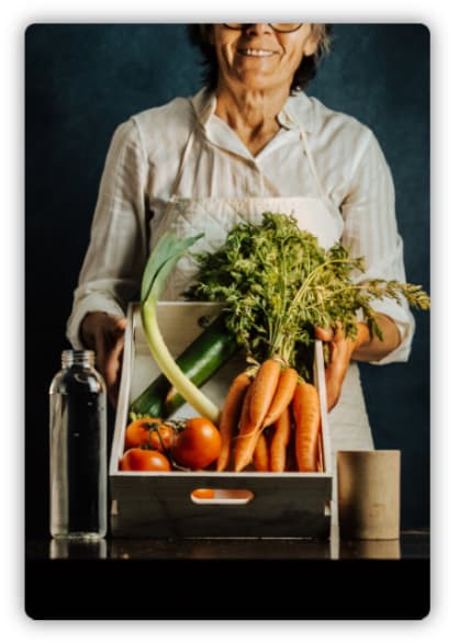 An old woman presenting a basket of vegetables including carrots, tomatoes, and zucchini