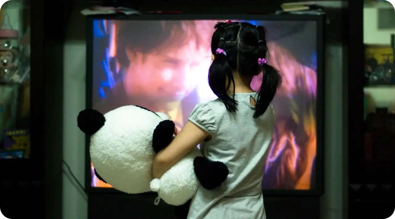 A little girl watching ott tv platform holding a stuffed panda